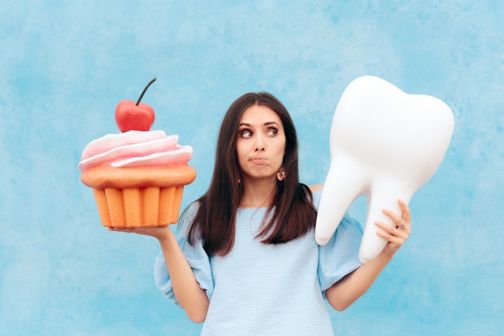 woman holding a sweet treat next to a tooth pondering 