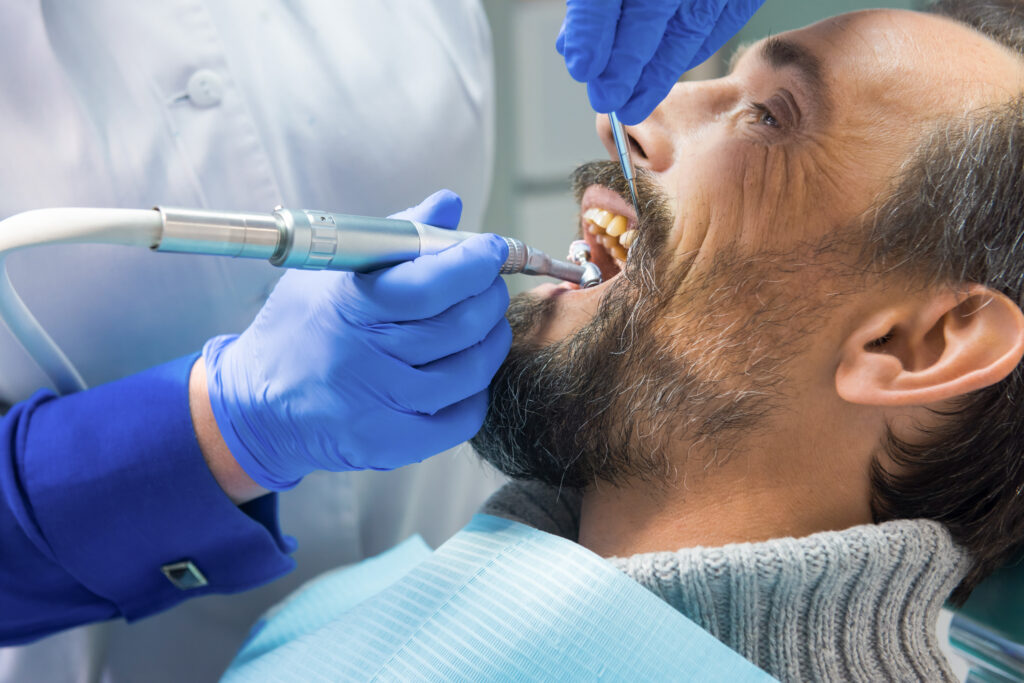 Man getting his cleaning done at a dentist with tools in his mouth